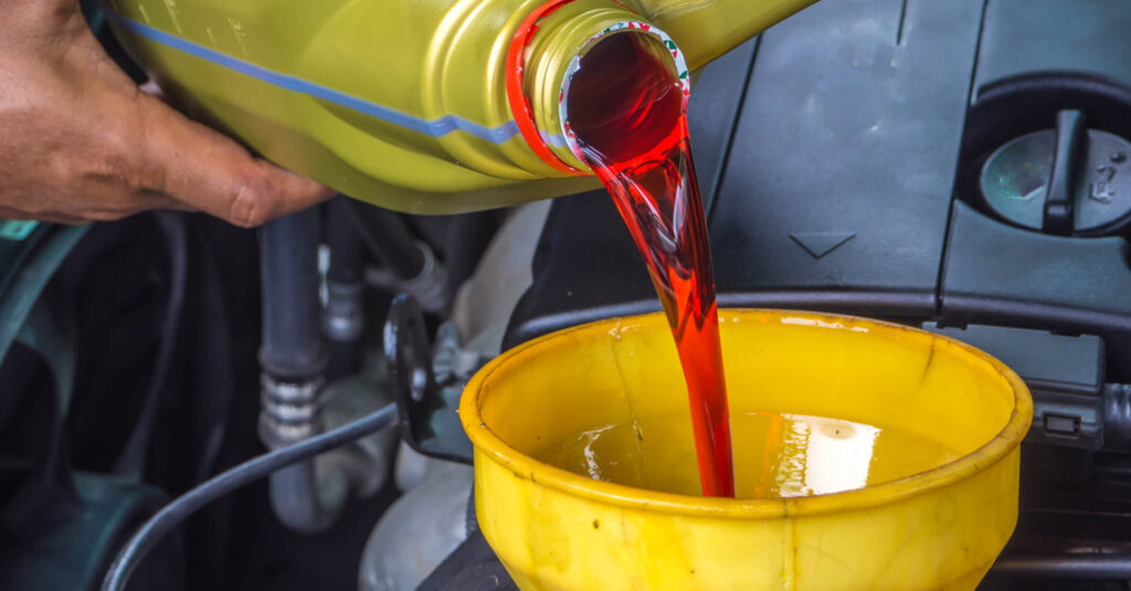 Pouring red transmission fluid into transmission using a yellow funnel