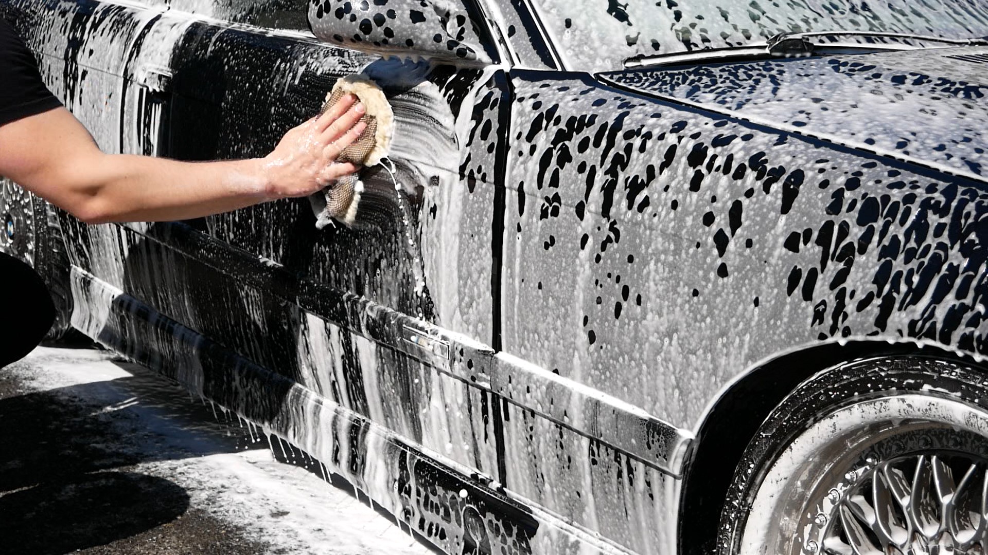 Person washing a black car that is covered in foam